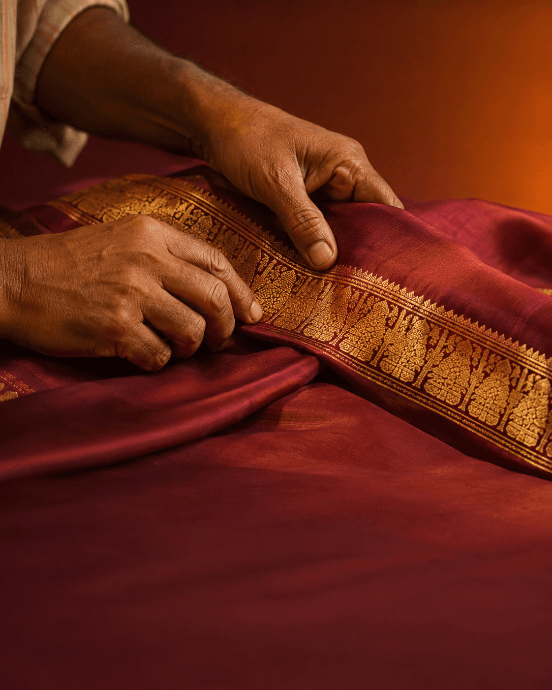A hand smoothing the zari border of a wine silk saree